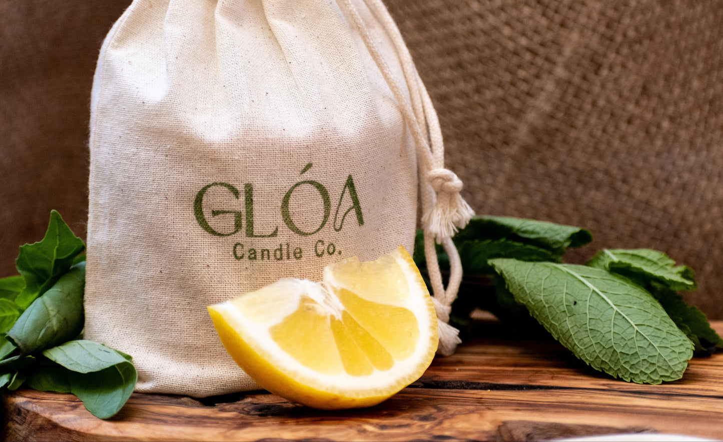 Drawstring bag with 'GLÓA Candle Co.' branding on a wooden surface with a lemon and leaves.