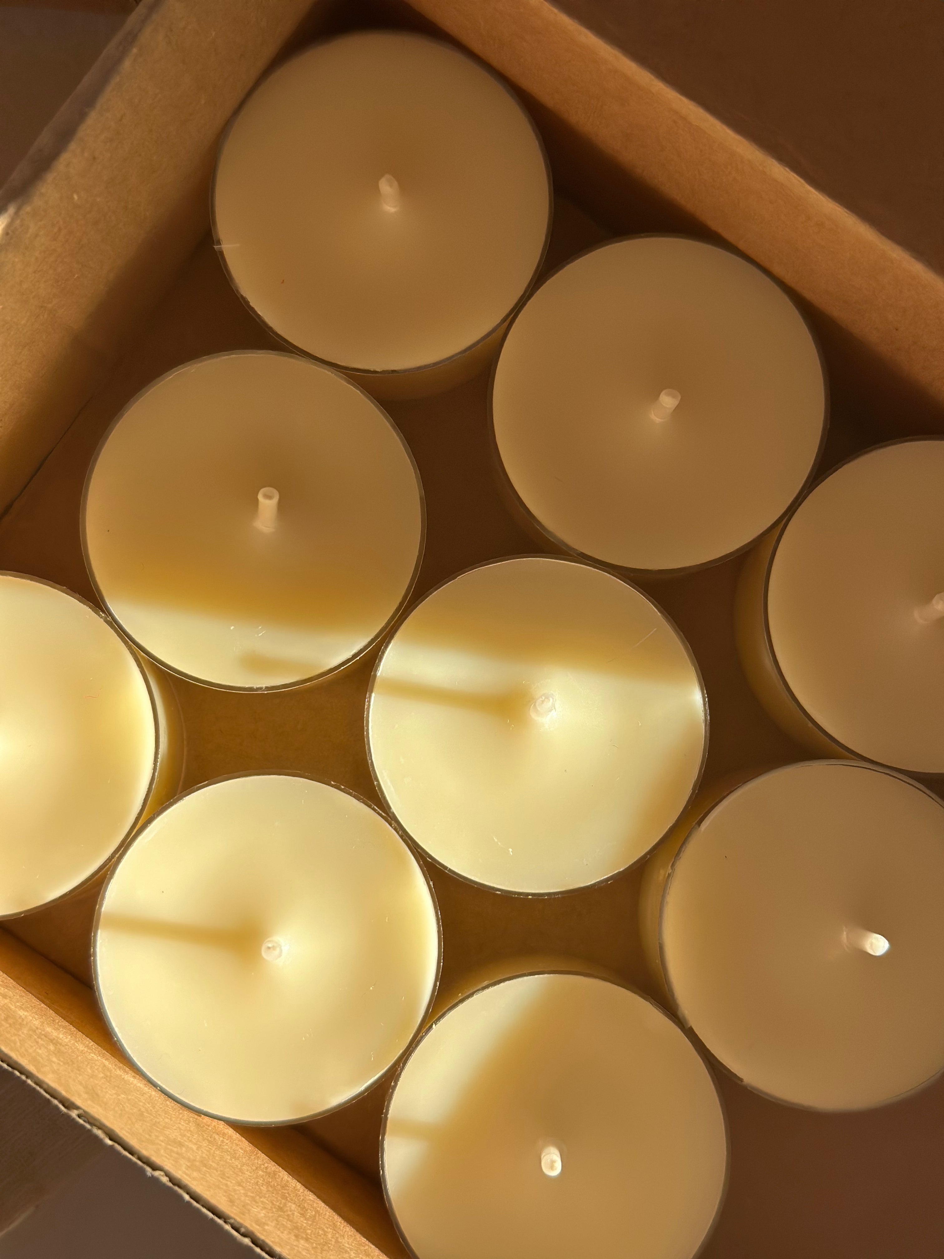 A zoomed in birdseye image of a box of white tealight candles in a brown cardboard box with sun light on them